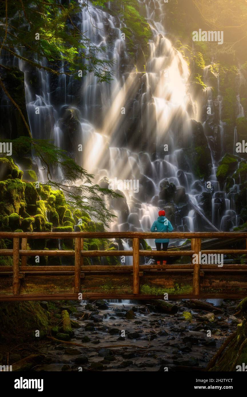 Escursionista su ponte di legno guardare la cascata, Ramona Falls, Oregon. Sunbeam attraversa la cascata e tocca il muschio Foto Stock