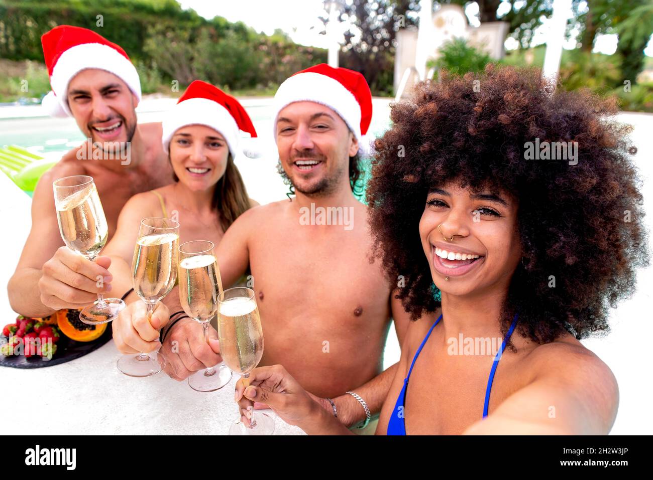 buon natale! felice gruppo di amici diversi che indossano natale santa hat avere champagne vino bevande a bordo piscina festa facendo un selfie festeggiamento Foto Stock