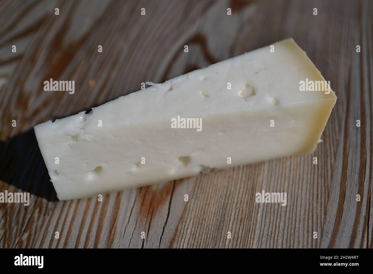 Pezzo di formaggio italiano duro su un pannello di legno con un bel modello della tessitura del legno nel sole. Foto Stock