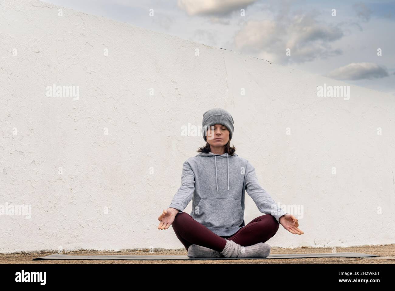 donna sportiva che indossa un cappello wolly, seduta a gambe incrociate e meditating fuori. Foto Stock