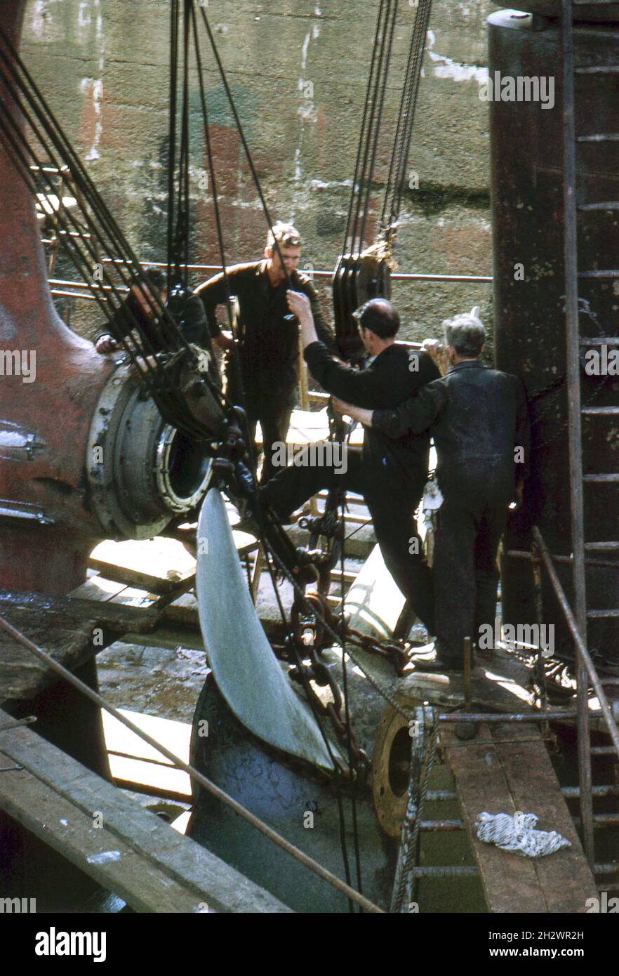 Ingegneri marini che sostituiscono l'elica di una nave in un bacino asciutto. Inizio degli anni '70. Foto Stock