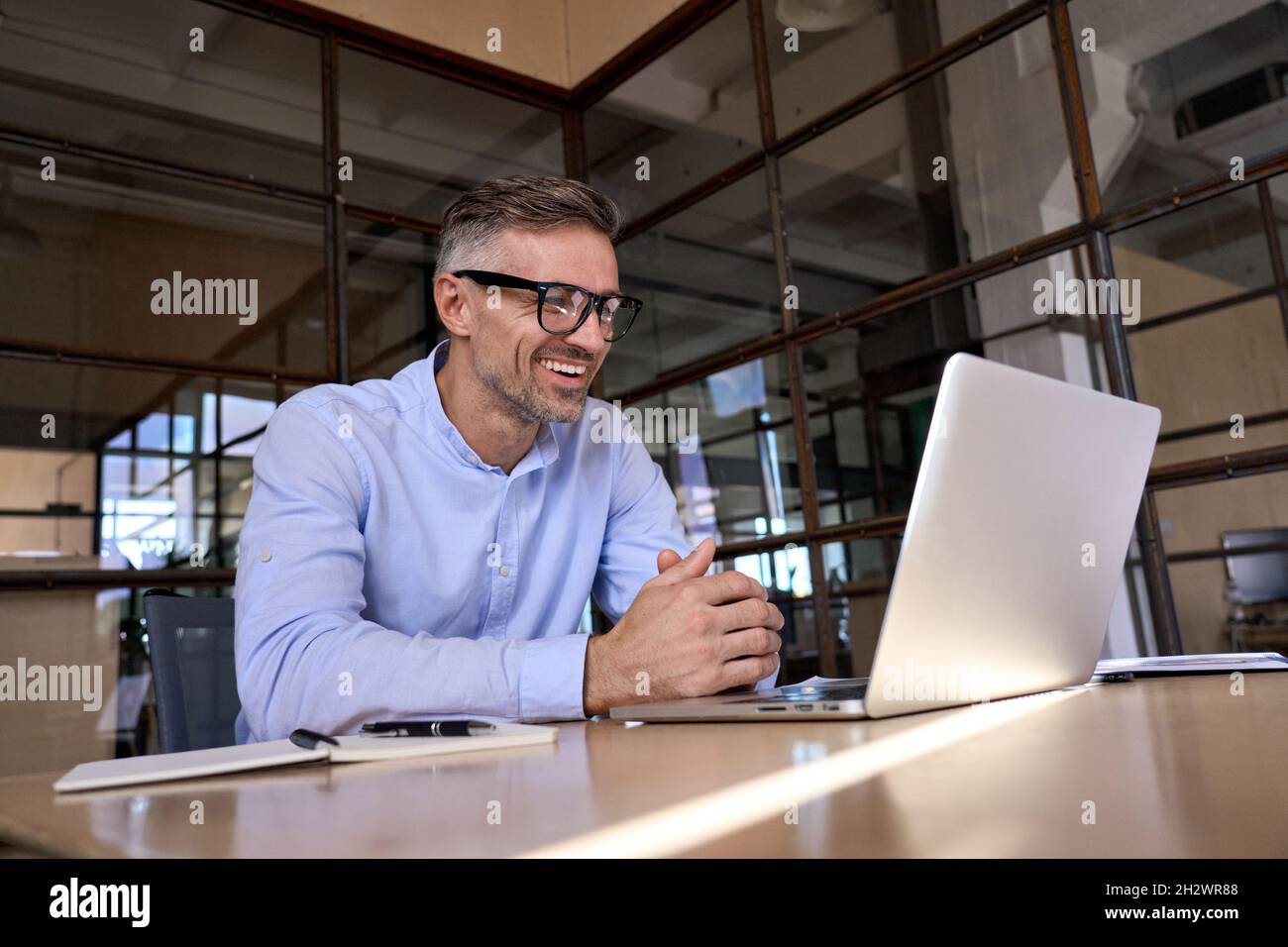 Un uomo d'affari felice e maturo che guarda un notebook che ha una riunione virtuale in ufficio. Foto Stock