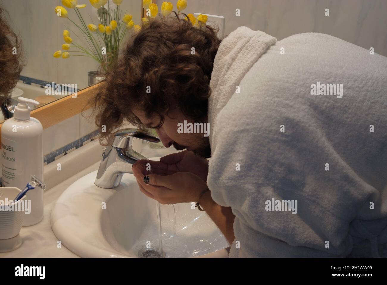 Il giovane in accappatoio si lava il viso nel lavandino del bagno prima di radersi. Home Spa Concept Beauty Concept. Foto Stock
