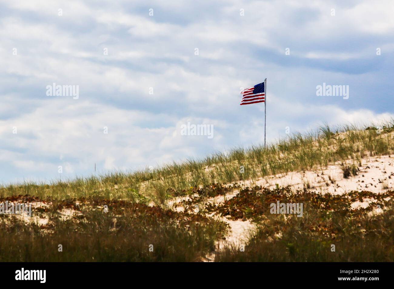 Bandiera americana su collina di erba sabbiosa alla luce del giorno con cielo nuvoloso Foto Stock