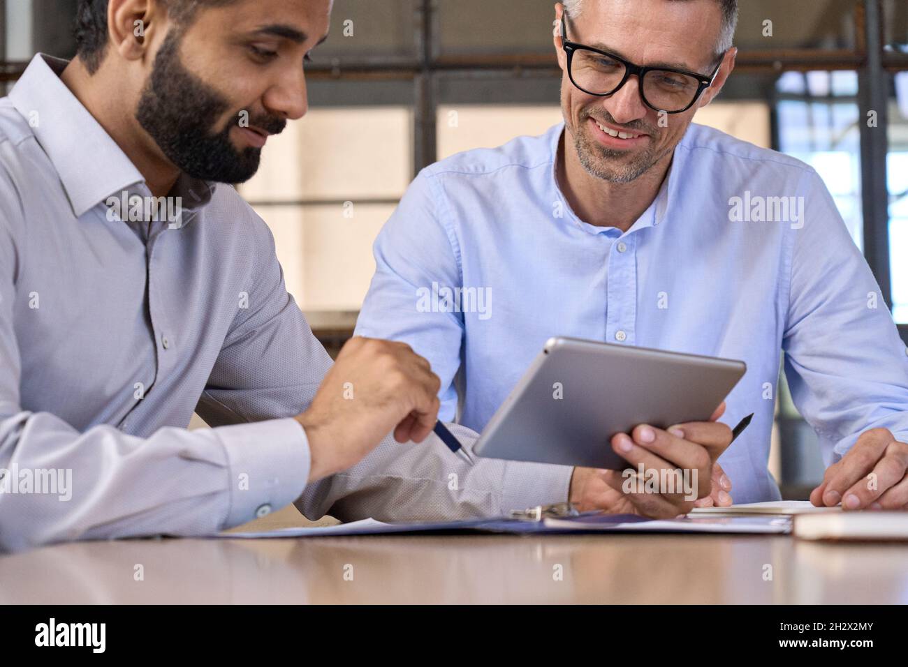 Due uomini d'affari soddisfatti e diversi che analizzano i dati finanziari utilizzando un tablet digitale. Foto Stock
