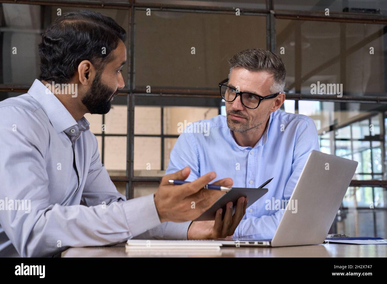 Due uomini d'affari diversi che parlano dei dati di mercato utilizzando un notebook e un tablet digitale. Foto Stock
