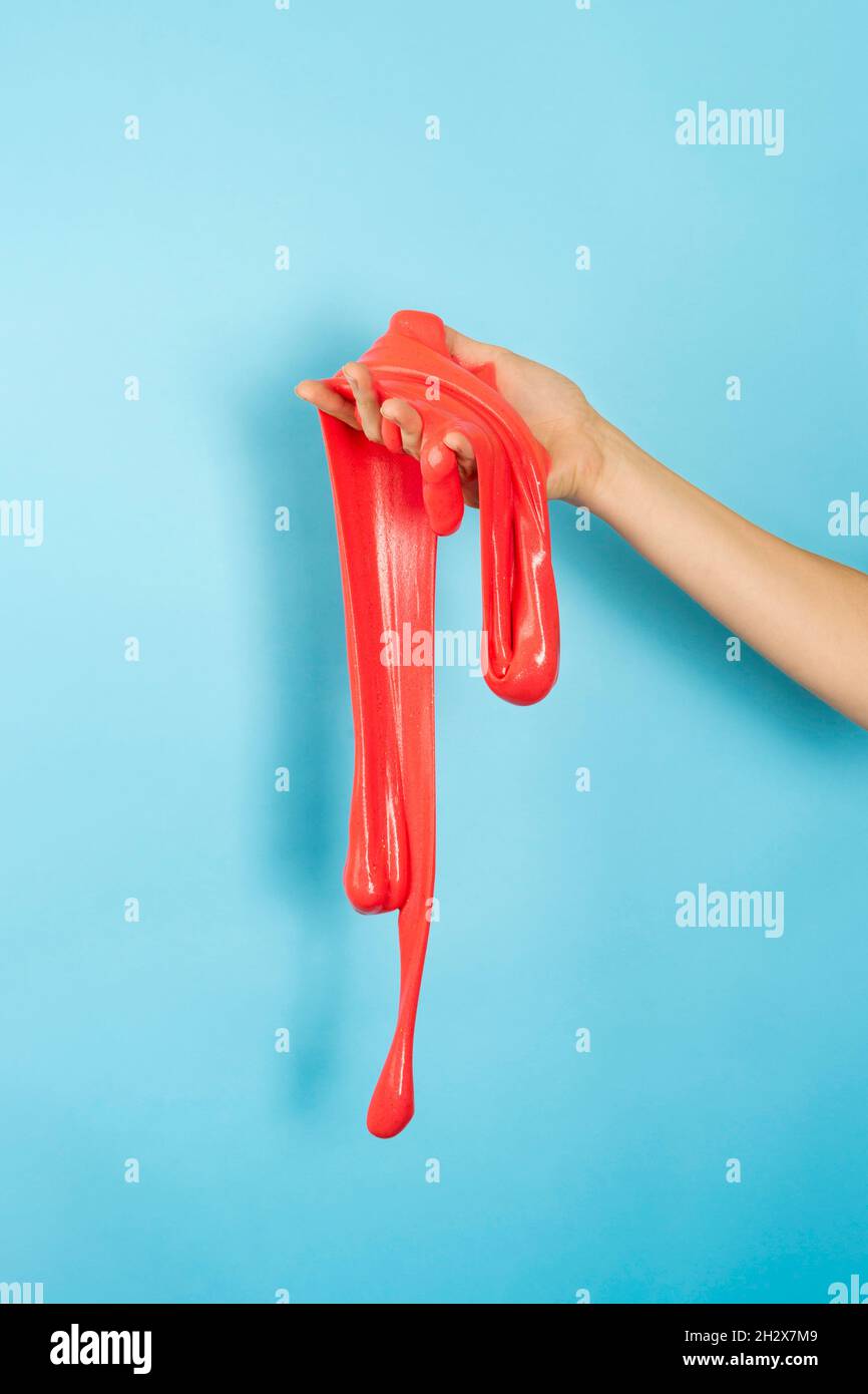 Primo piano su rosso lucido o corallo slime nella mano isolato su sfondo blu. Concetto di divertimento e di stress. Banner verticale Foto Stock