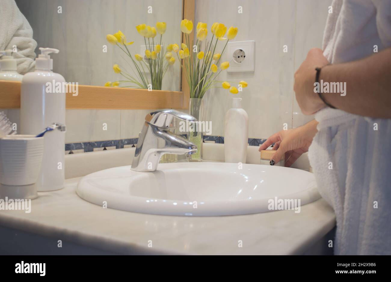 Il giovane uomo in accappatoio in bagno raccoglie la crema per il viso dal lavandino dopo la rasatura. Home Spa Beauty Concept. Foto Stock