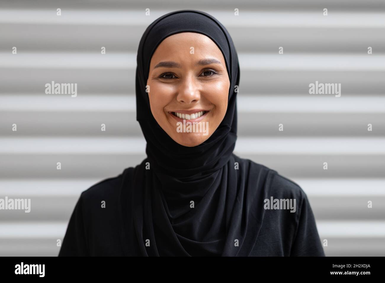 Ritratto di giovane donna araba sorridente che indossa Hijab nero in posa all'aperto Foto Stock