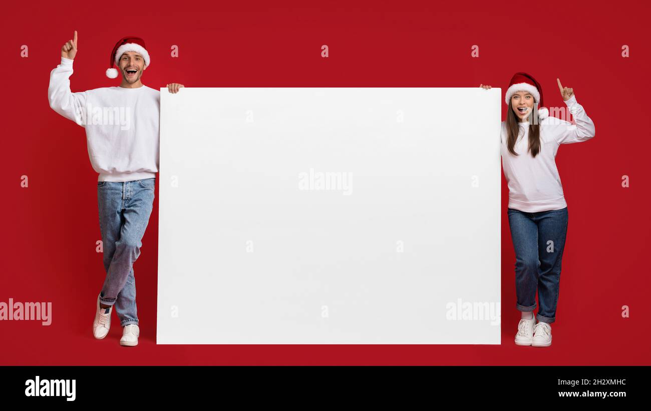 Idee per le vacanze. Coppia felice in Santa cappelli Holding Big Blank Advertisement Board Foto Stock