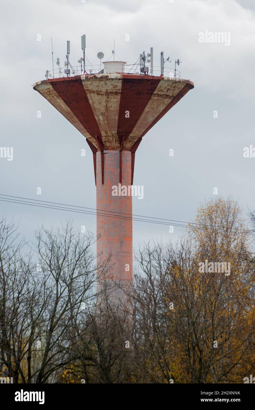 Una vecchia torre d'acqua marrone dotata di TV moderna, radio e antenne internet in autunno. Foto Stock