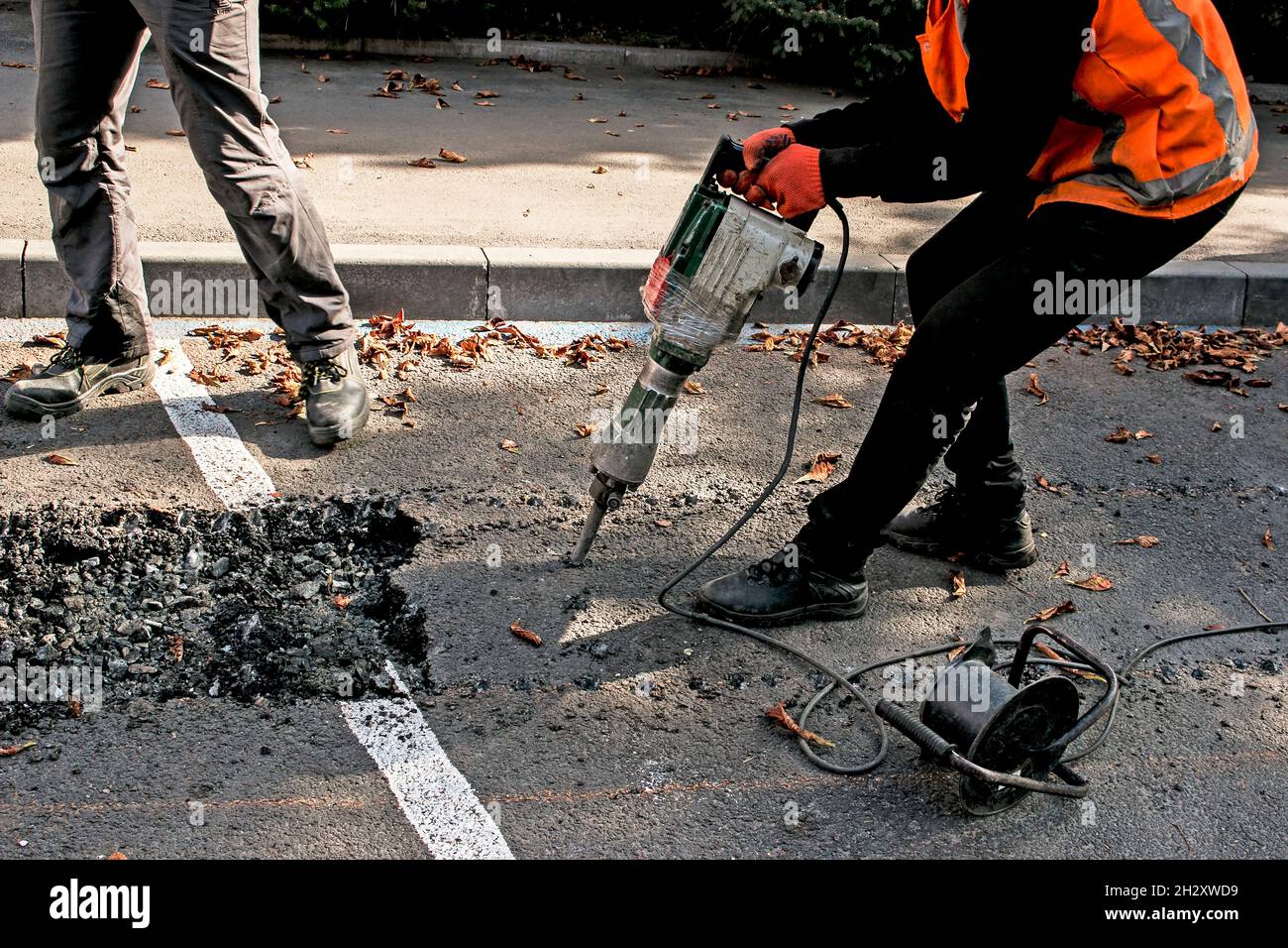 I lavoratori rimuovono uno strato di asfalto vecchio con un martello pneumatico in autunno. Lavori di costruzione su strada. Foto Stock