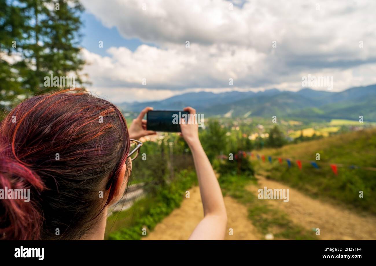 Vista posteriore della donna che tiene lo smartphone in entrambe le mani durante l'escursione, scattare foto per blog di viaggio, cercare un nuovo percorso online, cercare la connessione Foto Stock