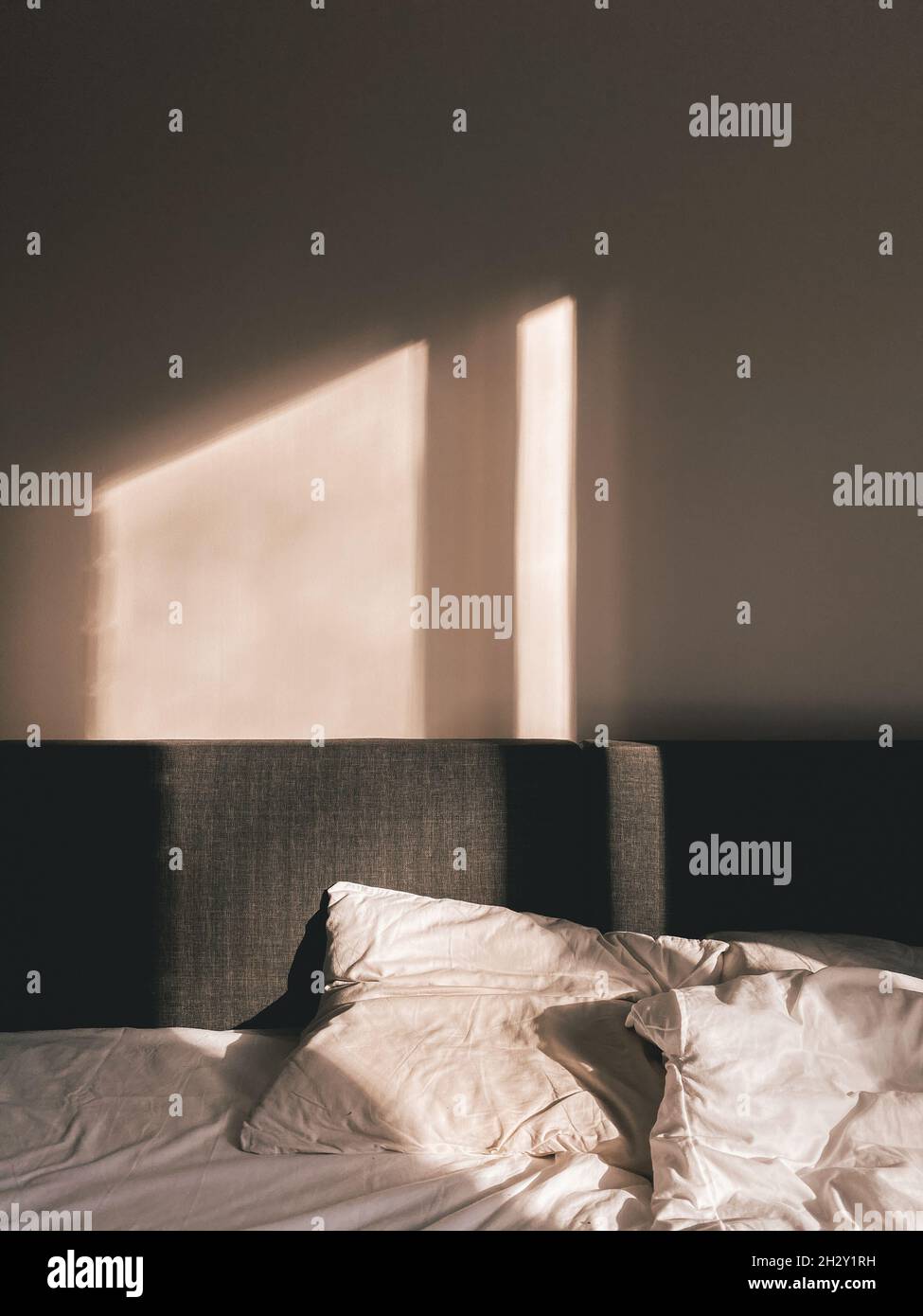 Idillio della camera da letto con un letto grigio e cuscini bianchi sui quali la luce d'autunno brilla dalla finestra Foto Stock