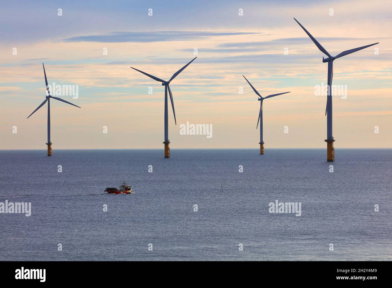 Piccola barca da pesca oscura da enormi turbine eoliche al largo della costa nord-orientale, Redcar, North Yorkshire, Inghilterra, Regno Unito. Foto Stock