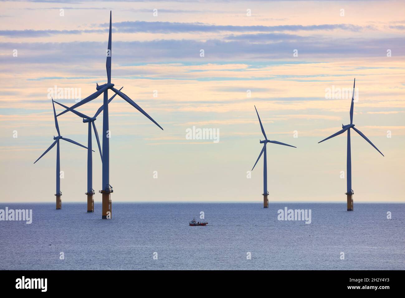 Piccola barca da pesca oscura da enormi turbine eoliche al largo della costa nord-orientale, Redcar, North Yorkshire, Inghilterra, Regno Unito. Foto Stock