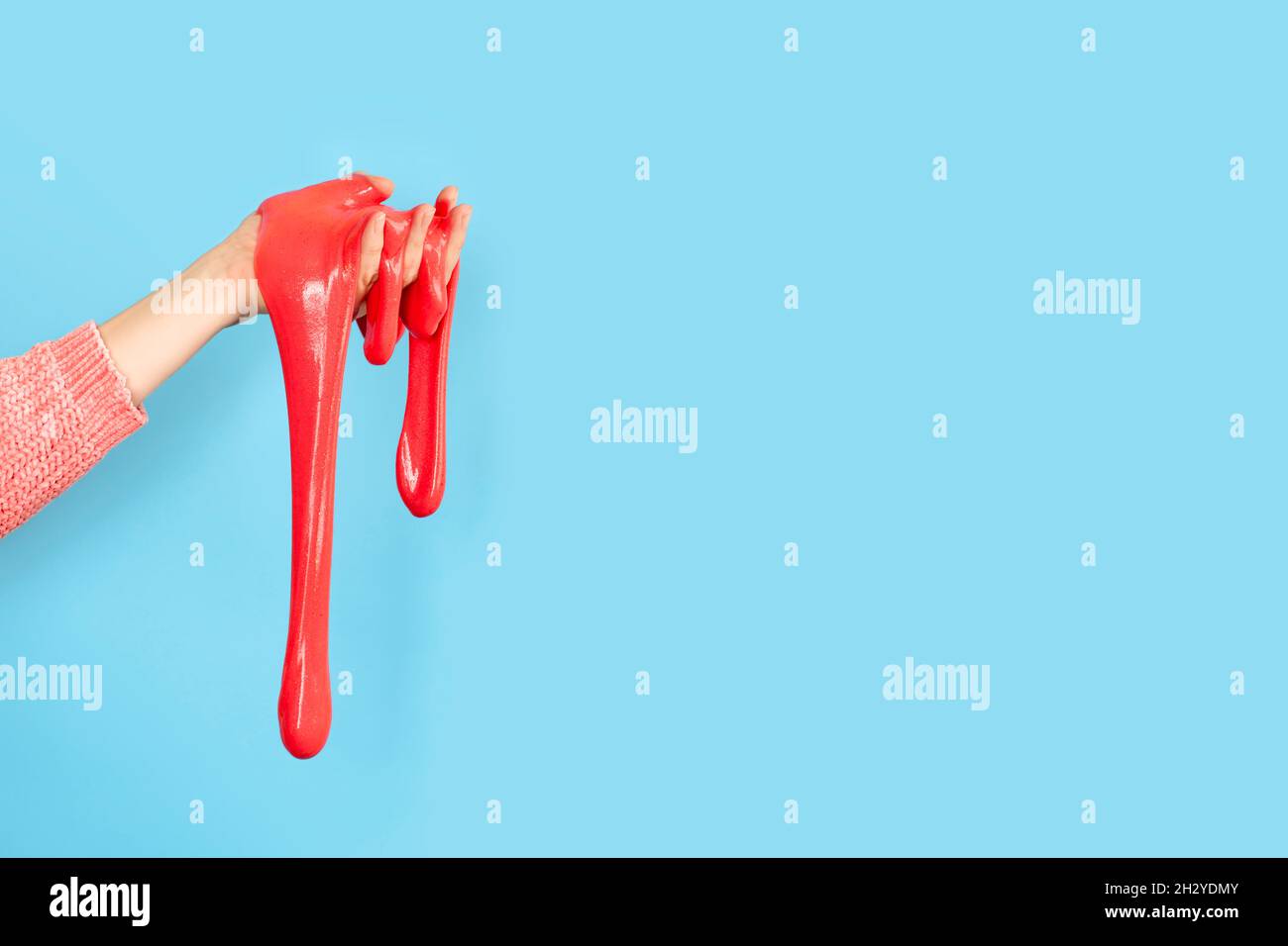 Primo piano su rosso lucido o corallo slime nella mano isolato su sfondo blu. Concetto di divertimento e di stress. Banner con spazio di copia Foto Stock