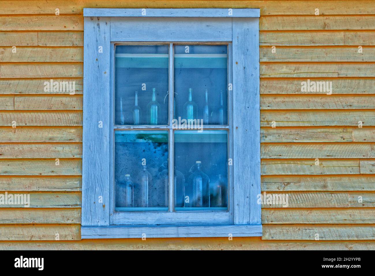 L'angolo superiore di un edificio di legno giallo. C'è una doppia finestra appesa con finiture bianche. Il bordo dell'edificio presenta un rivestimento bianco. Foto Stock