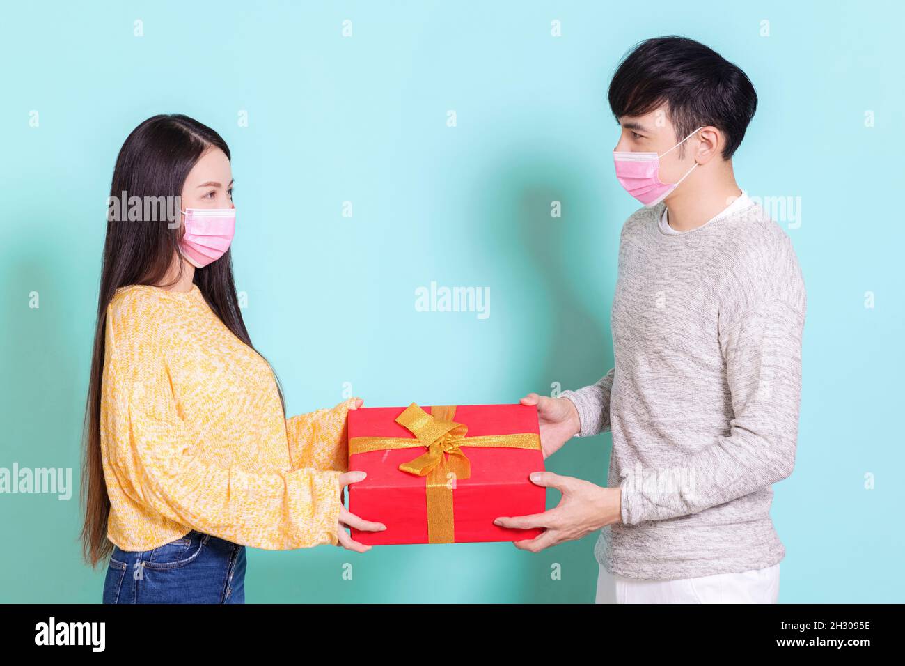 Felice giovane coppia che indossa maschere mediche dando regali durante la celebrazione di Natale. Isolato su sfondo blu Foto Stock