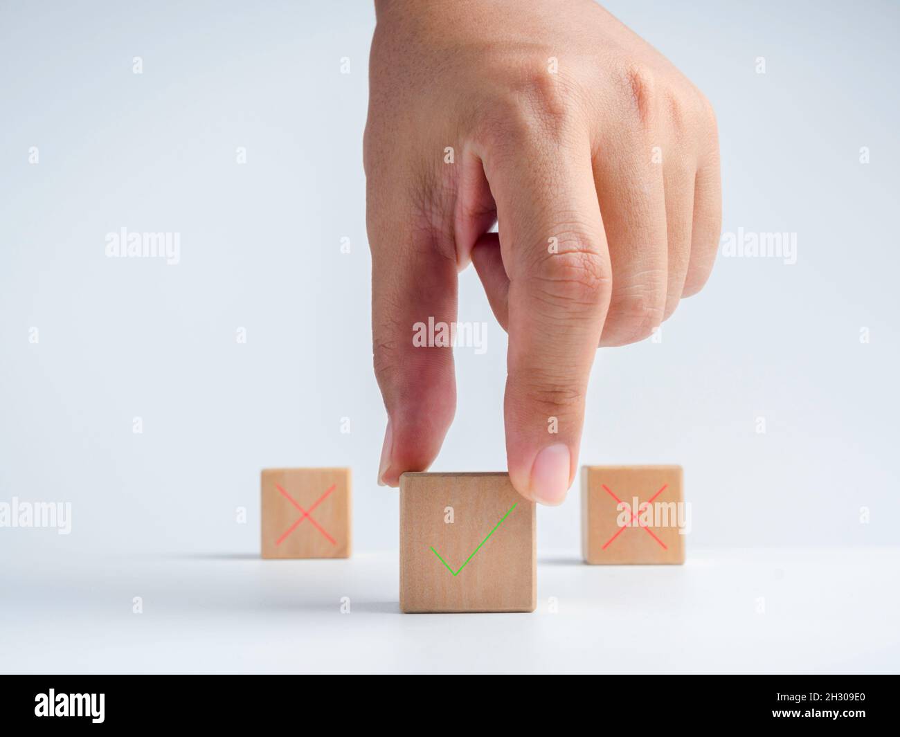 La mano dell'uomo d'affari sceglie l'un blocco di cubo di legno con la destra verde, segno di spunta icona di fronte al segno rosso della croce, segno errato icona blocchi sopra Foto Stock