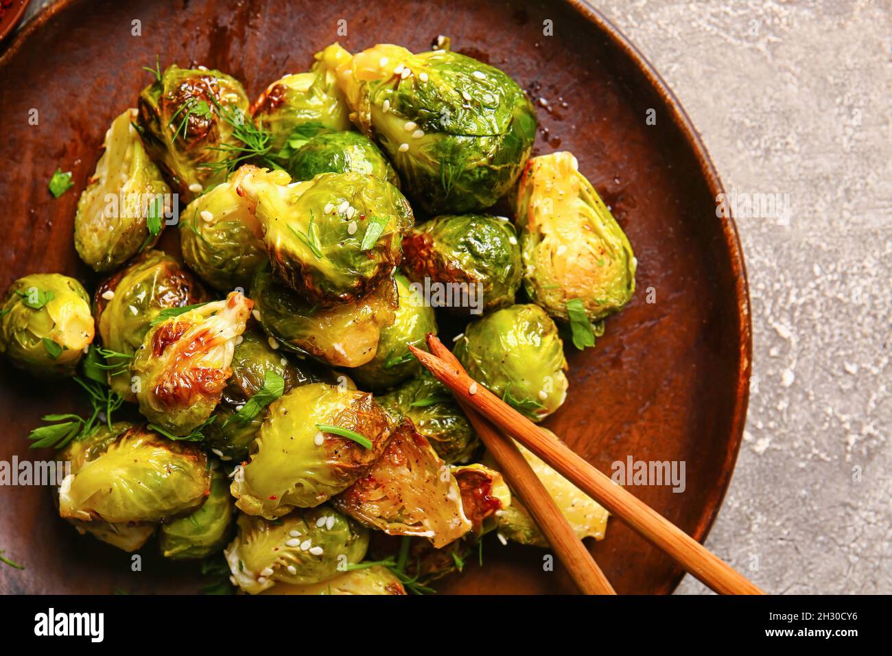 Piatto con delizioso cavolo di Bruxelles arrostito su sfondo grigio Foto Stock