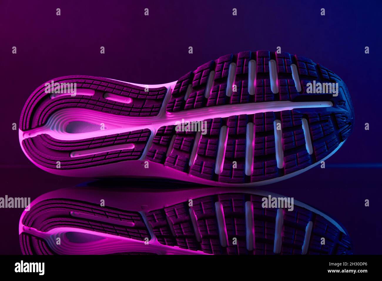 Suola di scarpe sportive con luci al neon. Scarpe da ginnastica ravvicinate su sfondo scuro. Concetto di stile di moda creativo Foto Stock