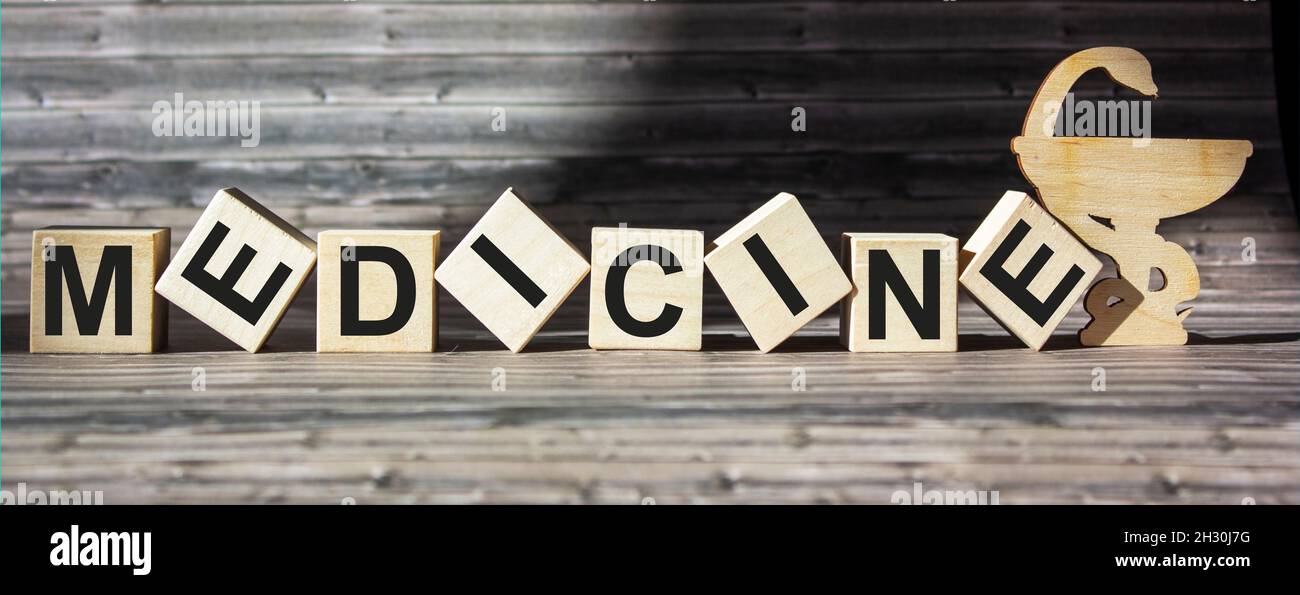 Parola di medicina scritta su blocchi su un tavolo di legno e un simbolo di medicina. Foto Stock