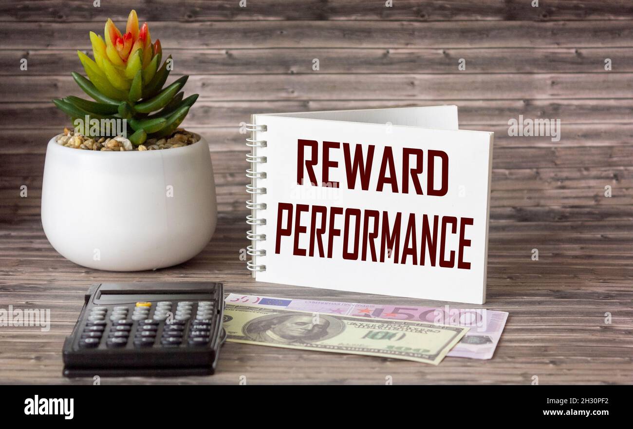 Concetto aziendale. Blocco note con il testo RICOMPENSA PERFORMANCE foglio di white paper per banconote, calcolatrice, cactus e banconote di dollari ed euro su un Foto Stock
