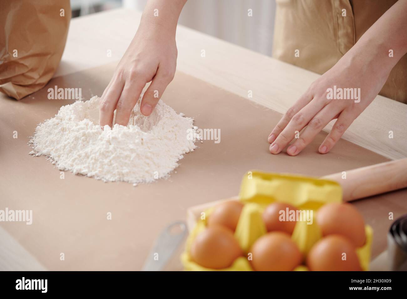Mani di donna che creano un pozzo al centro della farina per aggiungere l'uovo e mescolare l'impasto Foto Stock