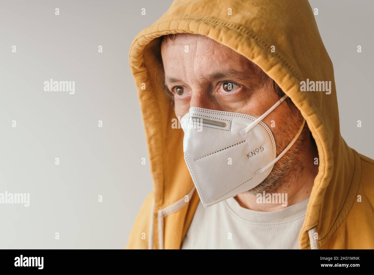 Uomo casual con giacca gialla con cappuccio indossare maschera respiratoria protettiva KN95 durante le pandemie covid-19, fuoco selettivo Foto Stock