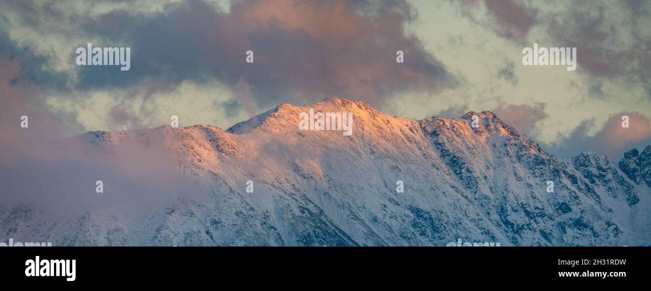 Panorama delle cime innevate della montagna alla luce del sole che tramonta Foto Stock