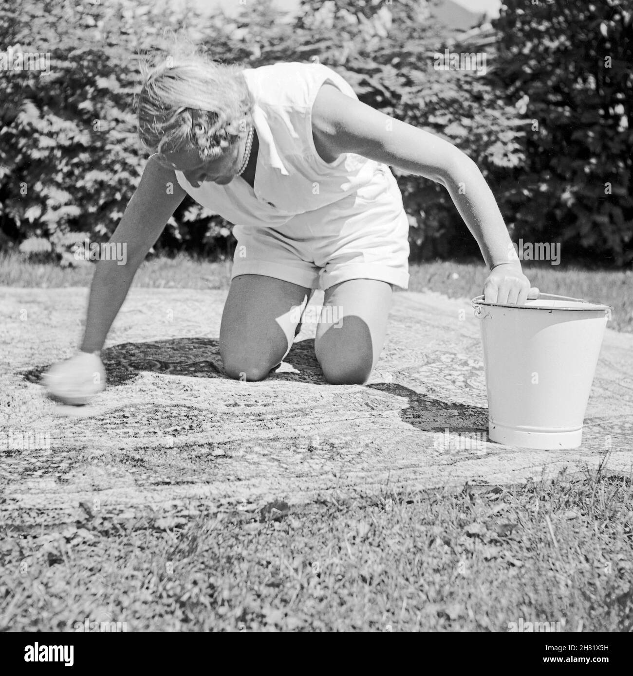 Eine Frau Hat im Garten den Teppich ausgebreitet um ihn zu reinigen, Deutschland 1958. Una donna ha portato un tappeto in giardino per pulirlo, Germania 1958. Foto Stock