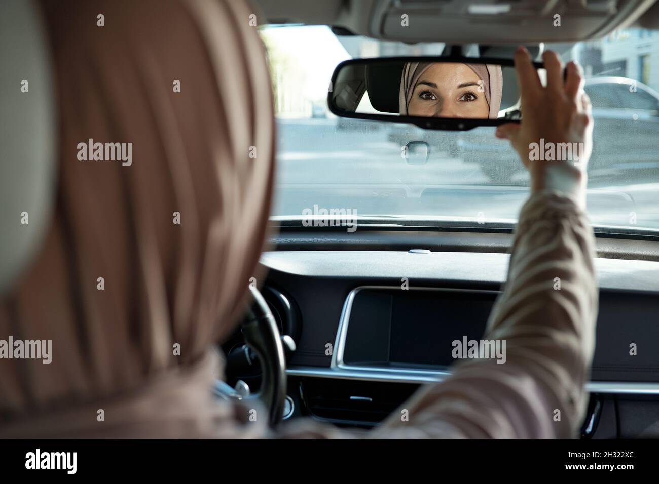 Riflessione della parte di faccia della femmina musulmana che lo guarda nello specchio mentre si siede all'interno della sua auto Foto Stock