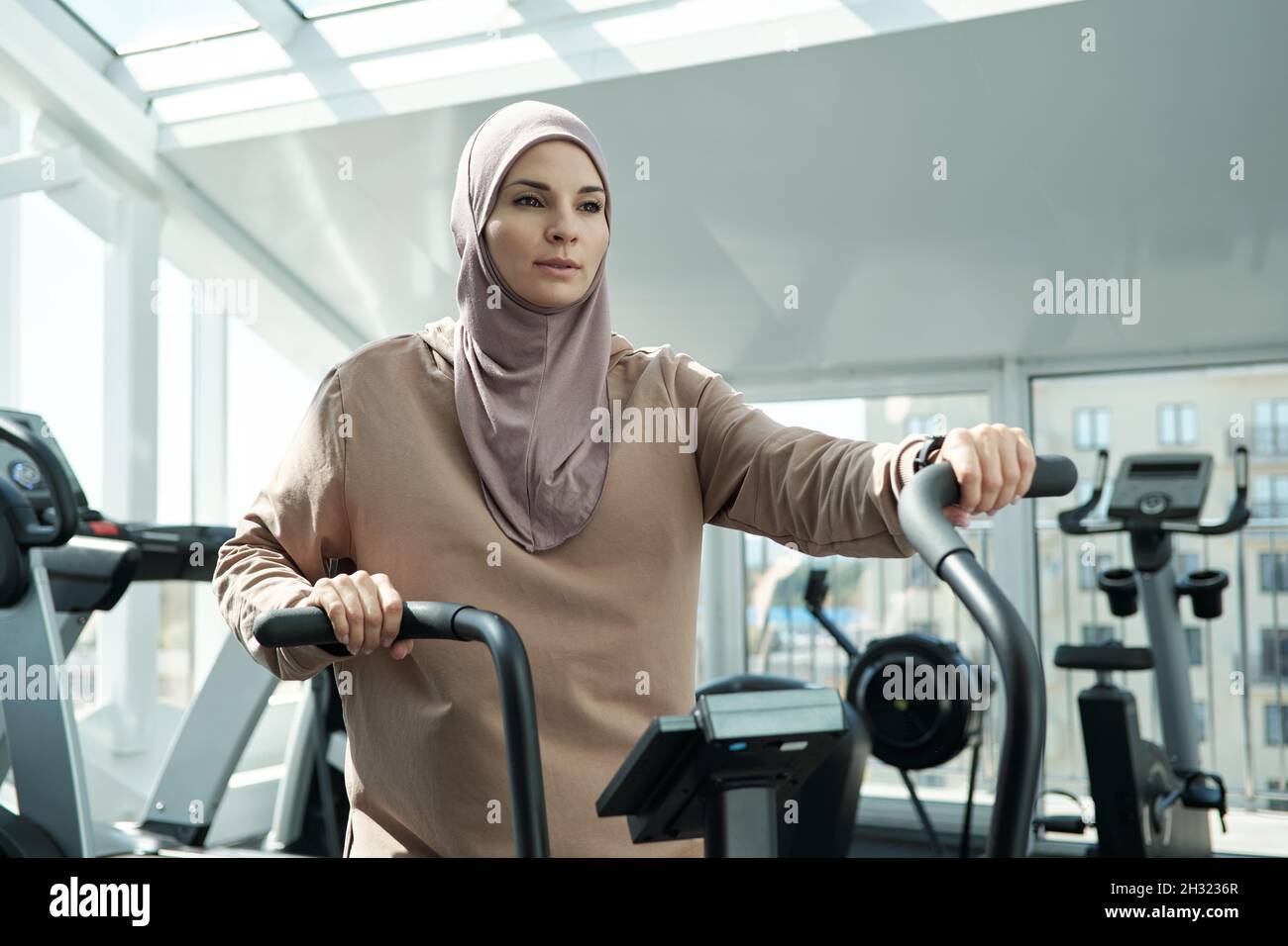 Giovane sportivo in hijab con maniglioni di attrezzature sportive mentre si esercita nel moderno centro fitness Foto Stock