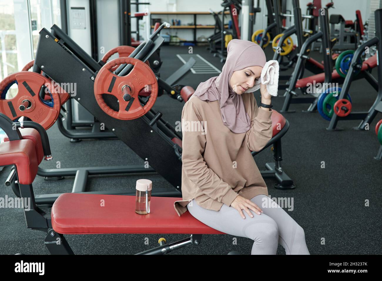 Giovane donna stanca in hijab e abbigliamento sportivo che riposa dopo un allenamento sportivo nel centro fitness Foto Stock