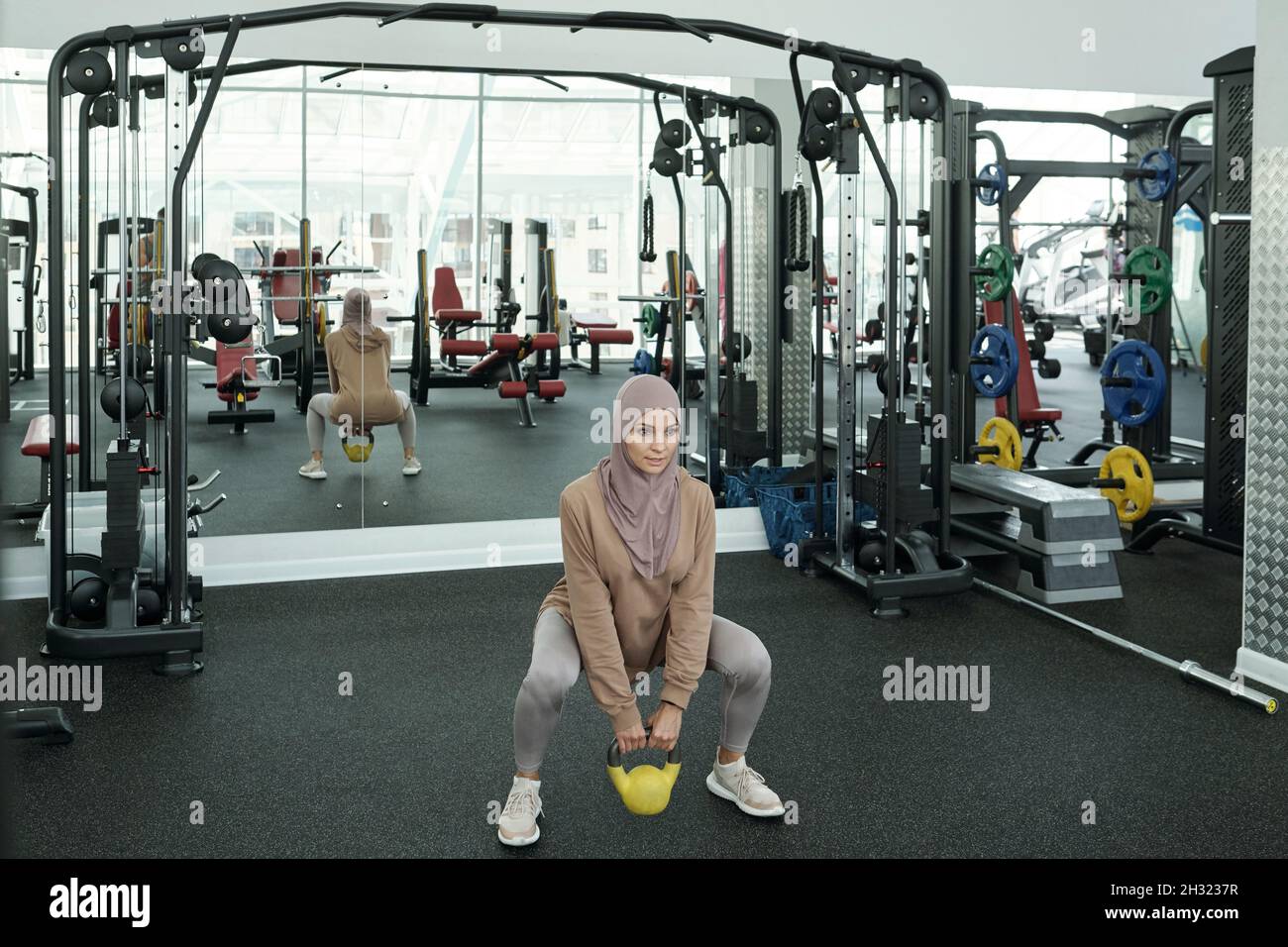 Giovane donna musulmana forte con peso pesante esercitandosi sulle gambe piegate del ginocchio in grande centro di idoneità Foto Stock