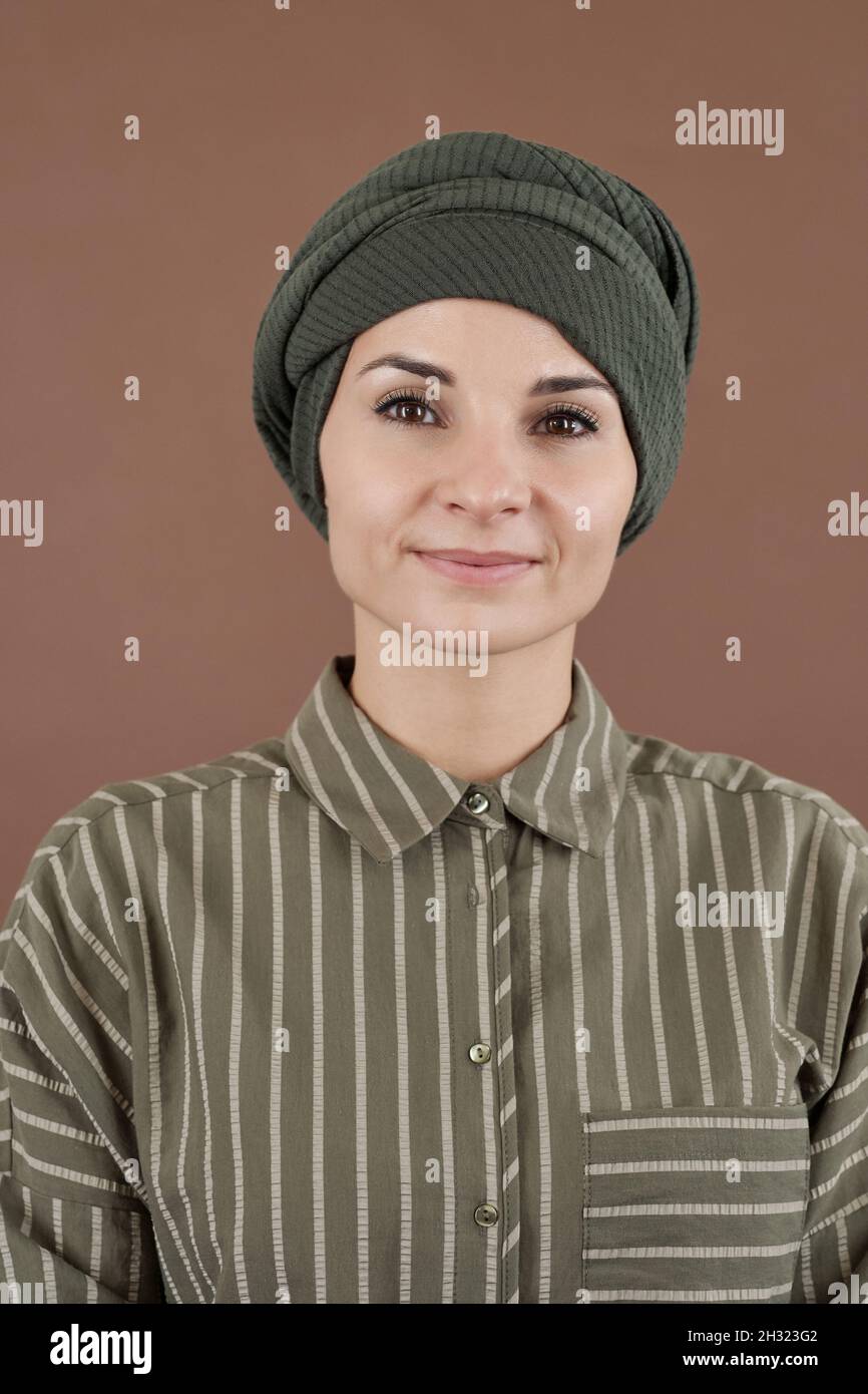 Felice giovane donna d'affari musulmana in headwrap e casualwear che vi guarda su sfondo marrone Foto Stock