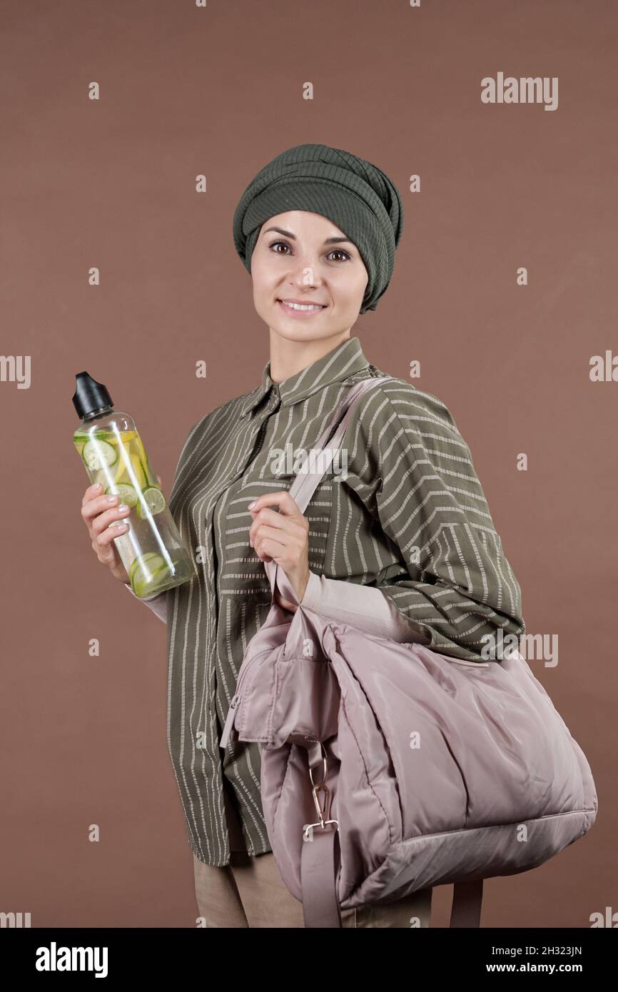 Felice giovane musulmana femmina con borsa e bottiglia di fresco sano cocktail in piedi di fronte alla macchina fotografica Foto Stock