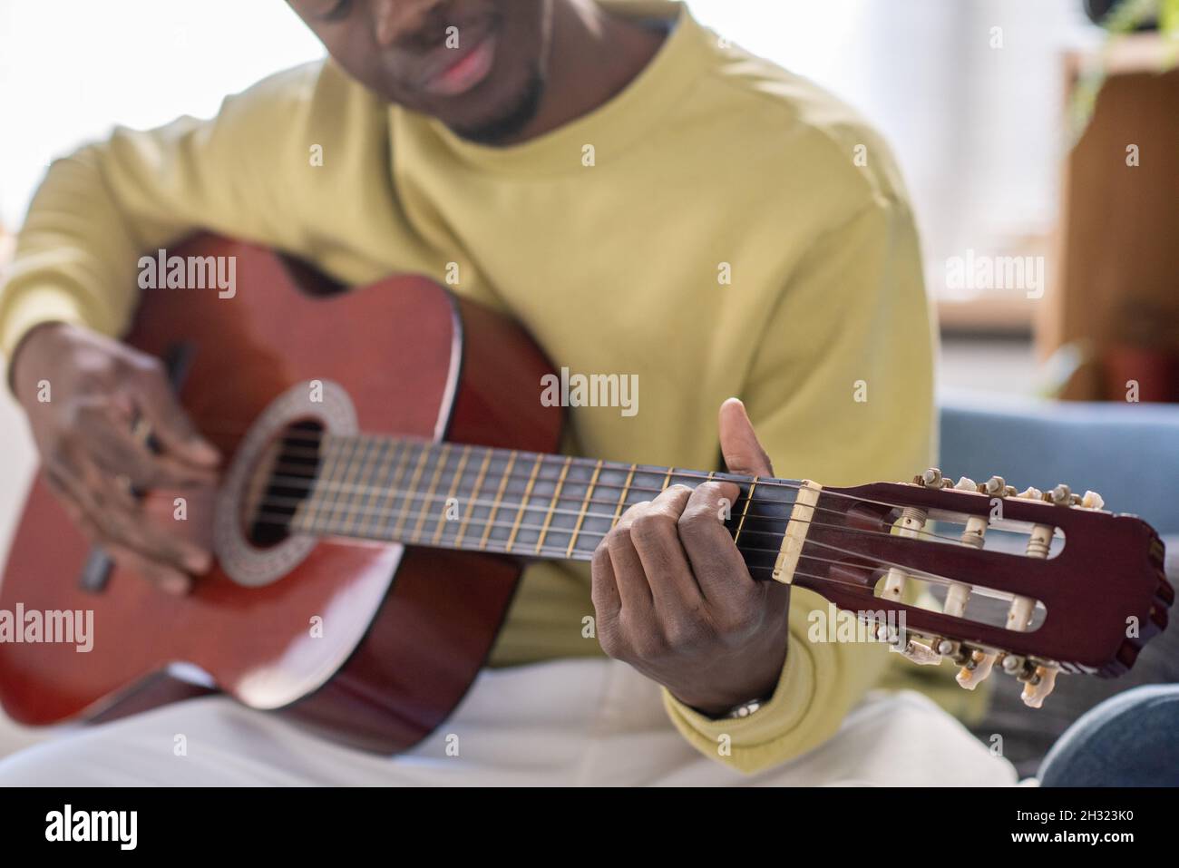 Mani di un giovane musicista africano che suona la chitarra di fronte alla macchina fotografica mentre insegnano il pubblico online Foto Stock