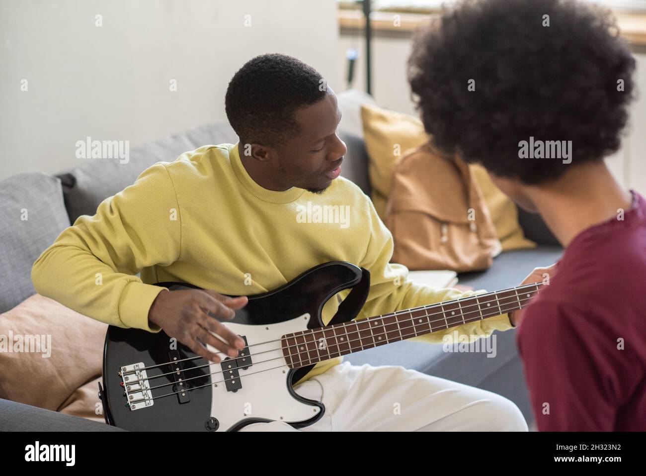 Giovane africano che insegna teenage interculturale ragazzo seduto davanti a lui come suonare la chitarra Foto Stock