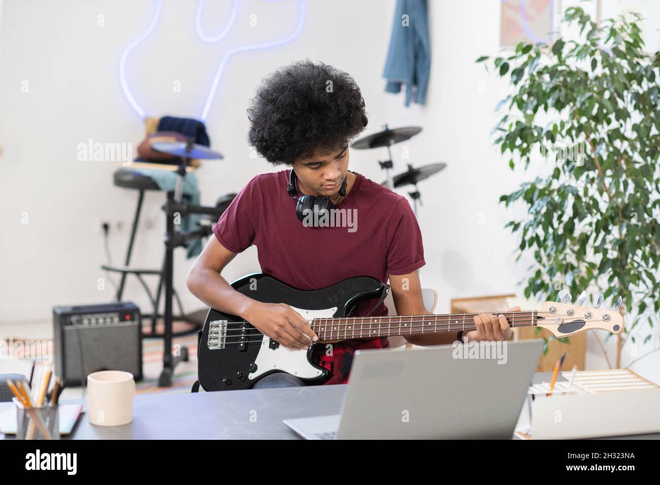 Ragazzo diligente che suona la chitarra elettrica di fronte al laptop durante una lezione online o una masterclass in ambiente domestico Foto Stock