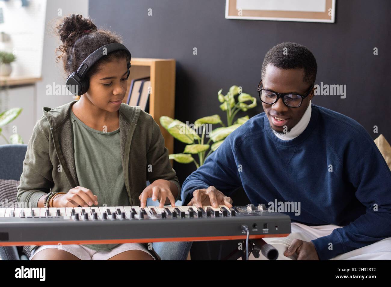 Ragazza biraciale carina in cuffie ripetendo dopo che la sua insegnante di musica tocca i tasti della tastiera del piano Foto Stock