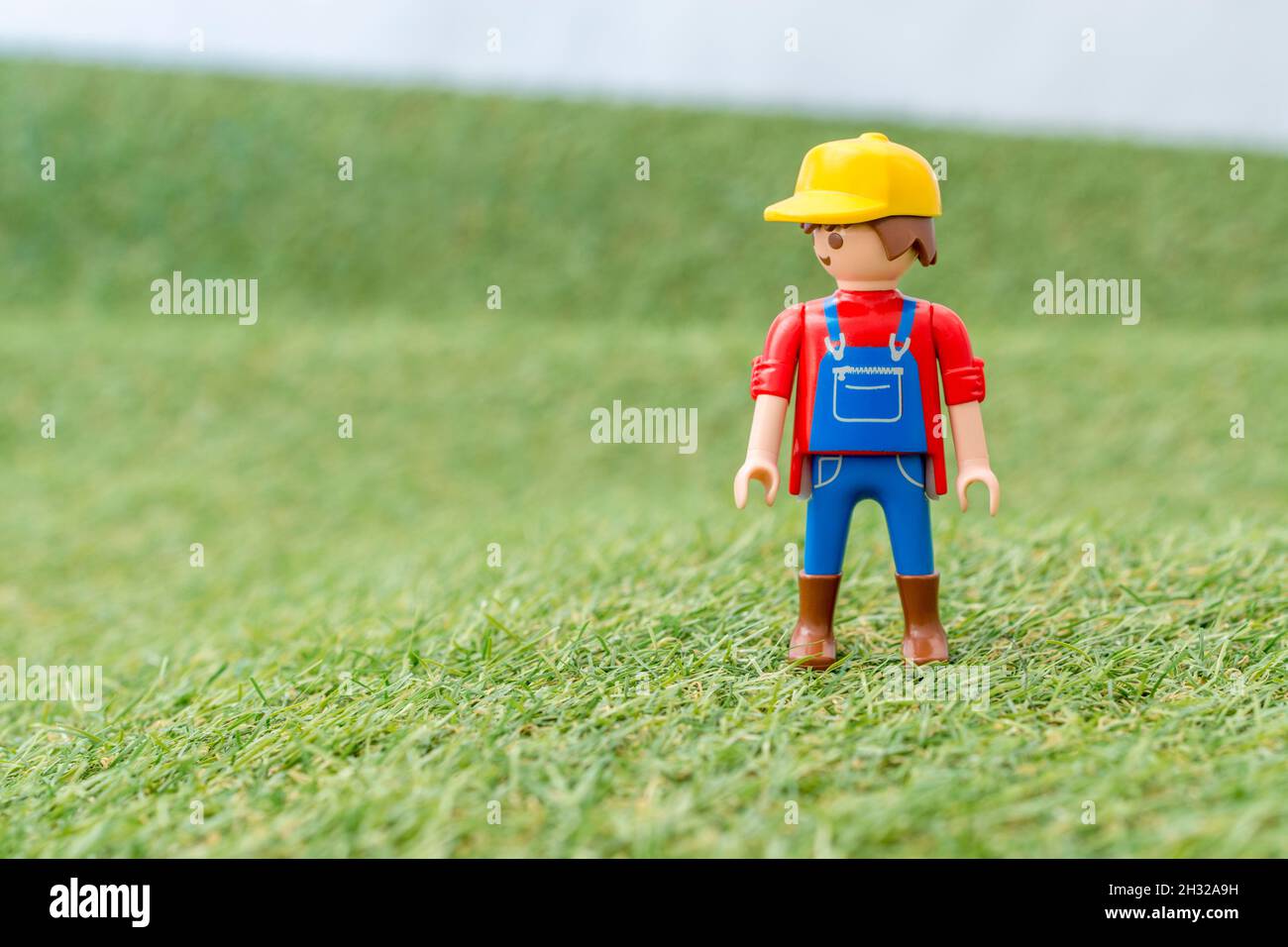 Piccolo giocattolo personaggio contadino Playmobil in piedi in 'campo' di faux / fake erba. Per la produzione di alimenti nel Regno Unito, da azienda agricola a forca, da campo a forca/da campo a piastra. Foto Stock