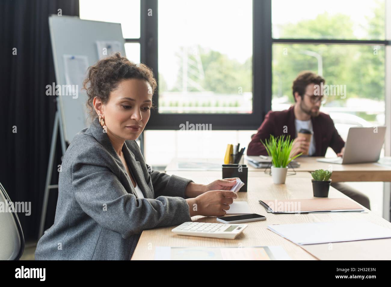 Donna d'affari afroamericana che guarda la calcolatrice vicino a smartphone e documenti in ufficio Foto Stock