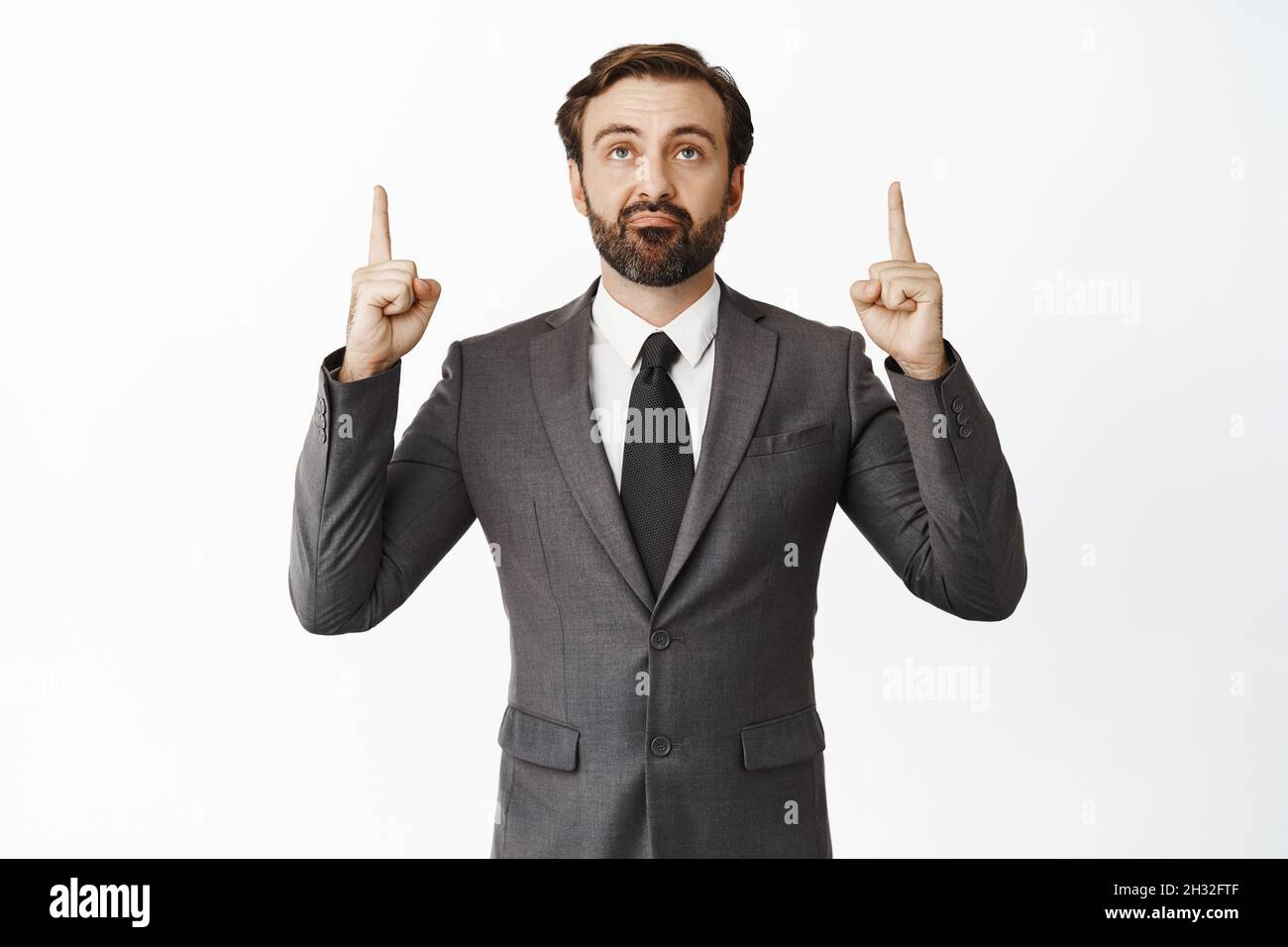 Scettico imprenditore maschio puntando le dita in su e guardando promo offerta, smirk con unamused, deluso volto espressione, in piedi su bianco Foto Stock