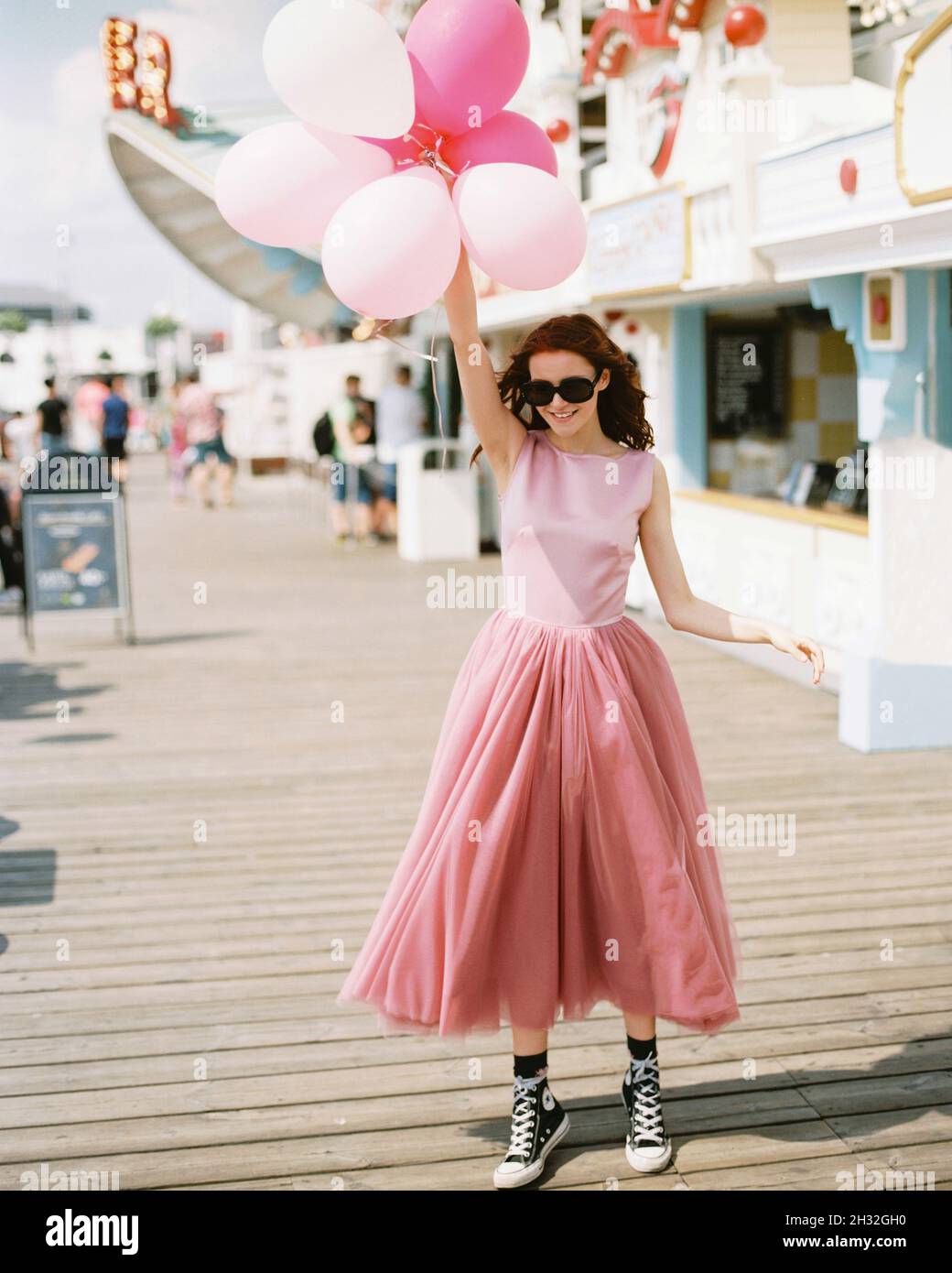 Ragazza felice con palloncini in abiti rosa promo al parco divertimenti. Adolescenti in abiti rosa sera in vacanza. Festa di compleanno idea. Foto Stock