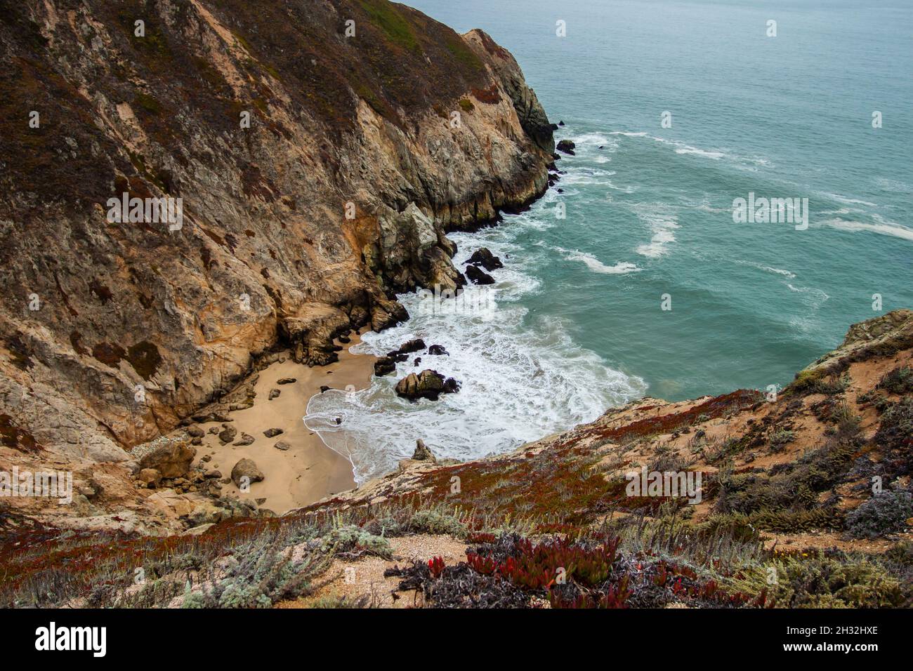 Bella spiaggia a baia con scogliere rocciose con erba e piante, acque blu e limpide dell'oceano e onde | viste panoramiche lungo la Pacific Coast Highway (Route 1) Foto Stock