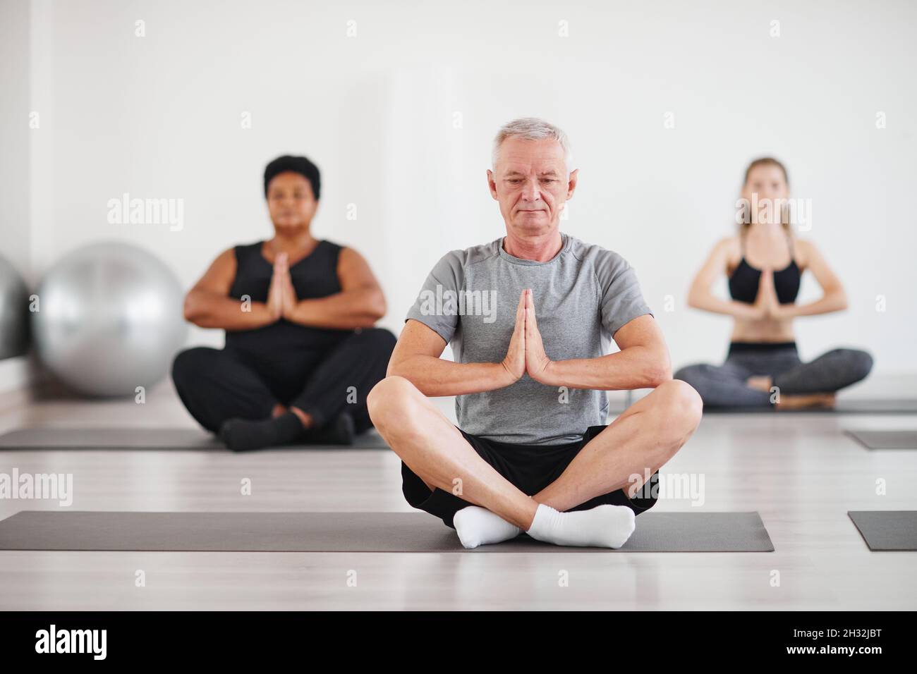 Ritratto di uomo anziano seduto in posizione lotus e meditando durante la lezione di yoga in studio Foto Stock