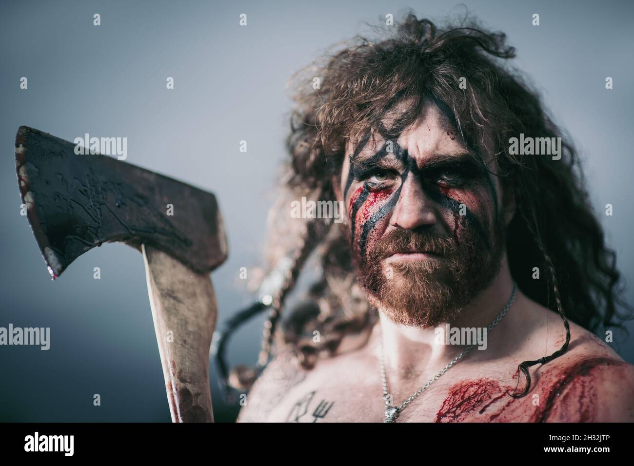 Ritratto vichingo guerriero medievale con tatuaggio sulla pelle, tagli sul corpo e trecce in capelli con armi per attaccare il nemico. Concept foto storica Foto Stock
