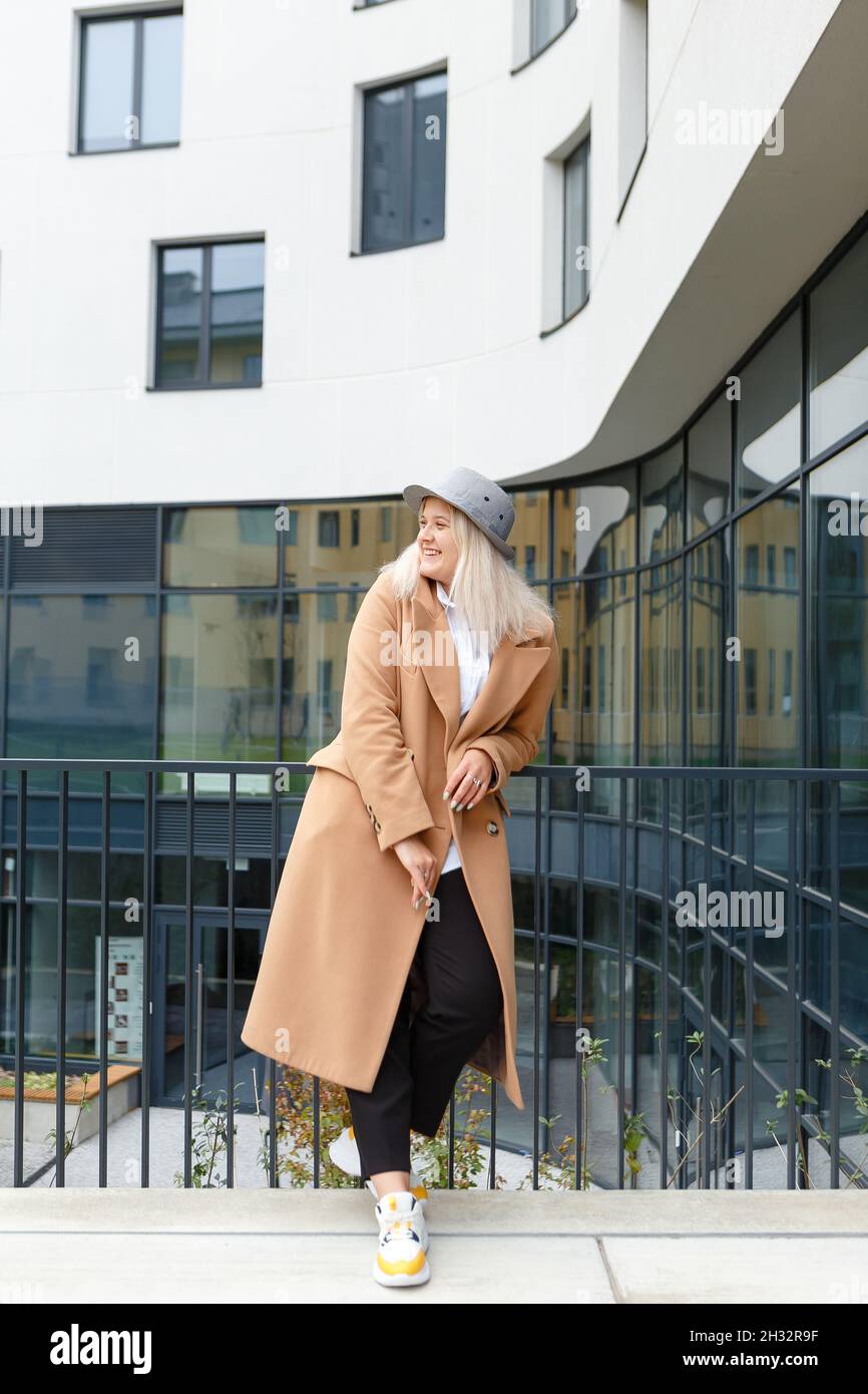giovane donna bionda in un cappotto beige e cappello sorridente Foto Stock
